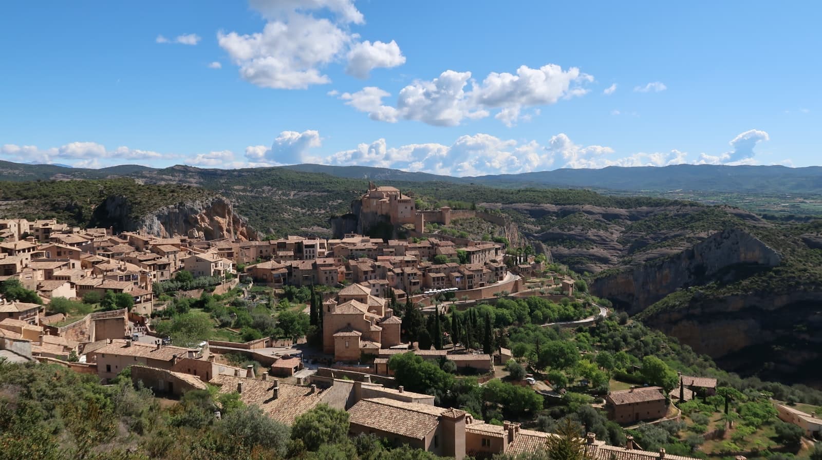 Alquézar — Ancient stone village nestled in a green valley under sky.