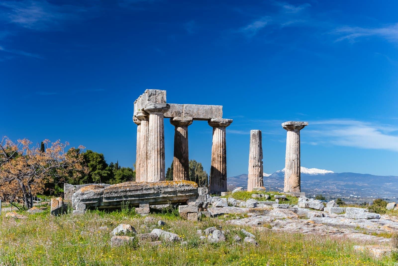 Ancient Corinth — gray concrete pillar on green grass field under blue sky during daytime