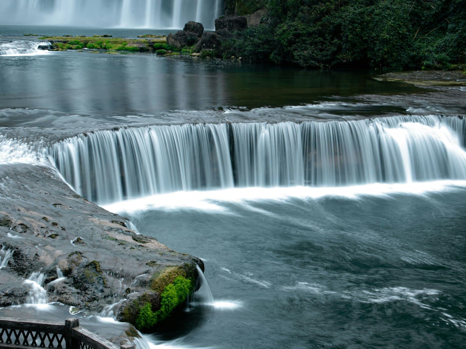 Anshun — A waterfall with a bridge over it next to a body of water