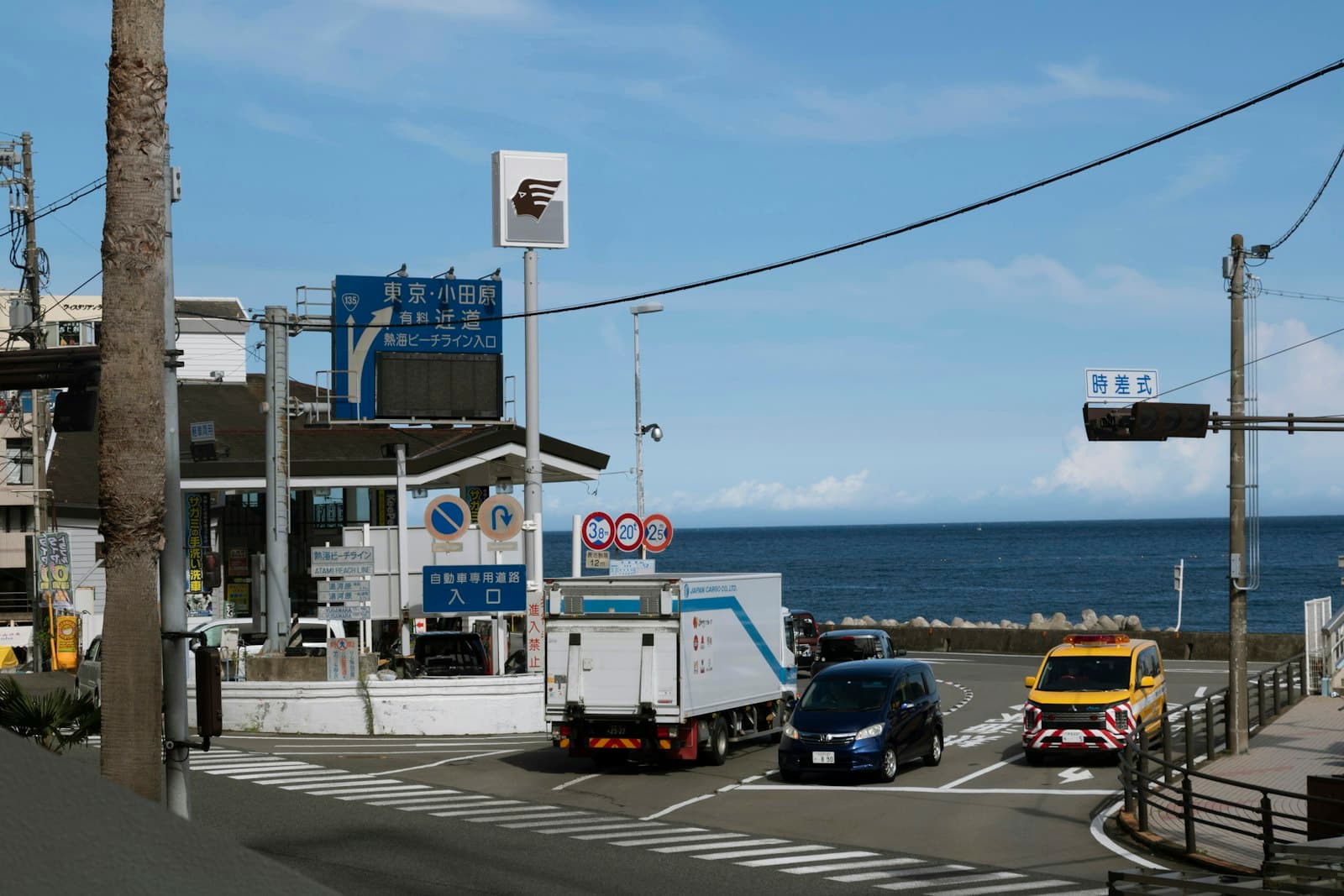 Atami — a couple of trucks driving down a street next to the ocean