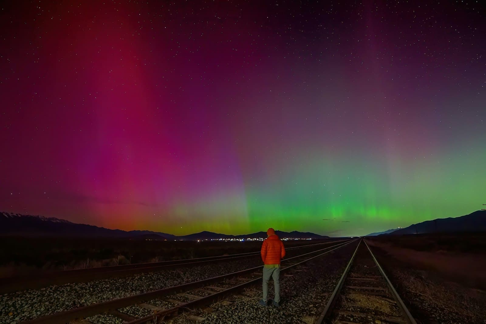 Aurora — a man standing on a train track under a colorful sky
