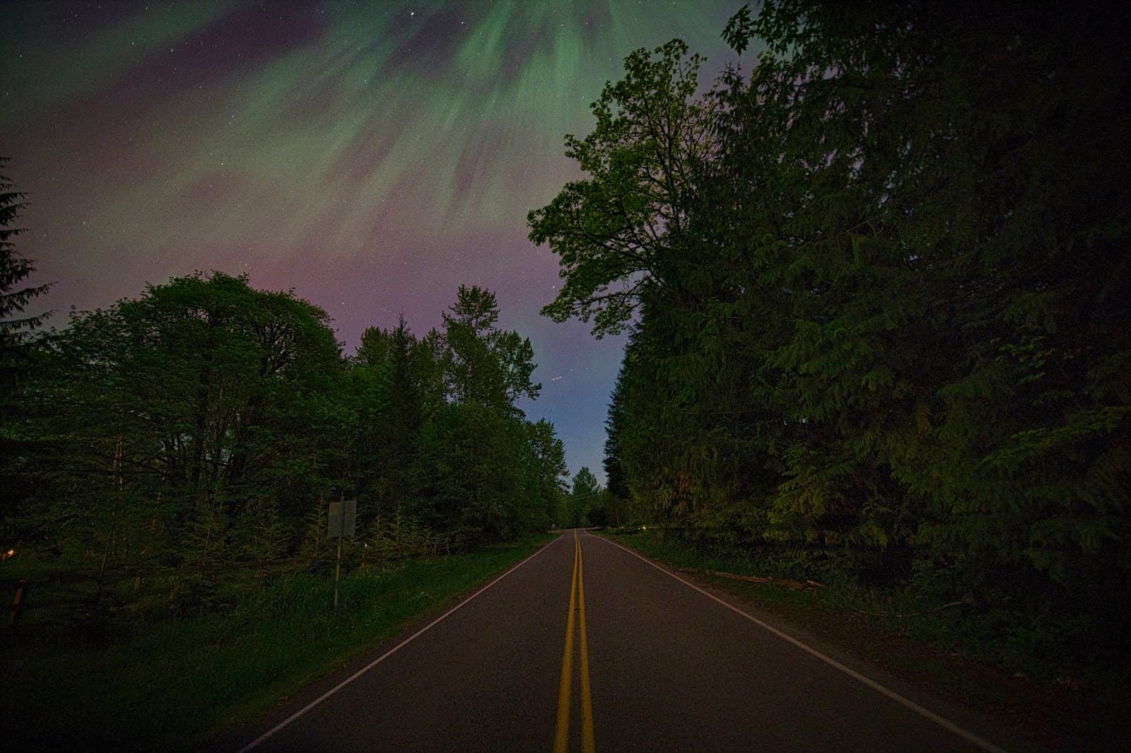Aurora — a long road with a green and purple aurora bore in the sky