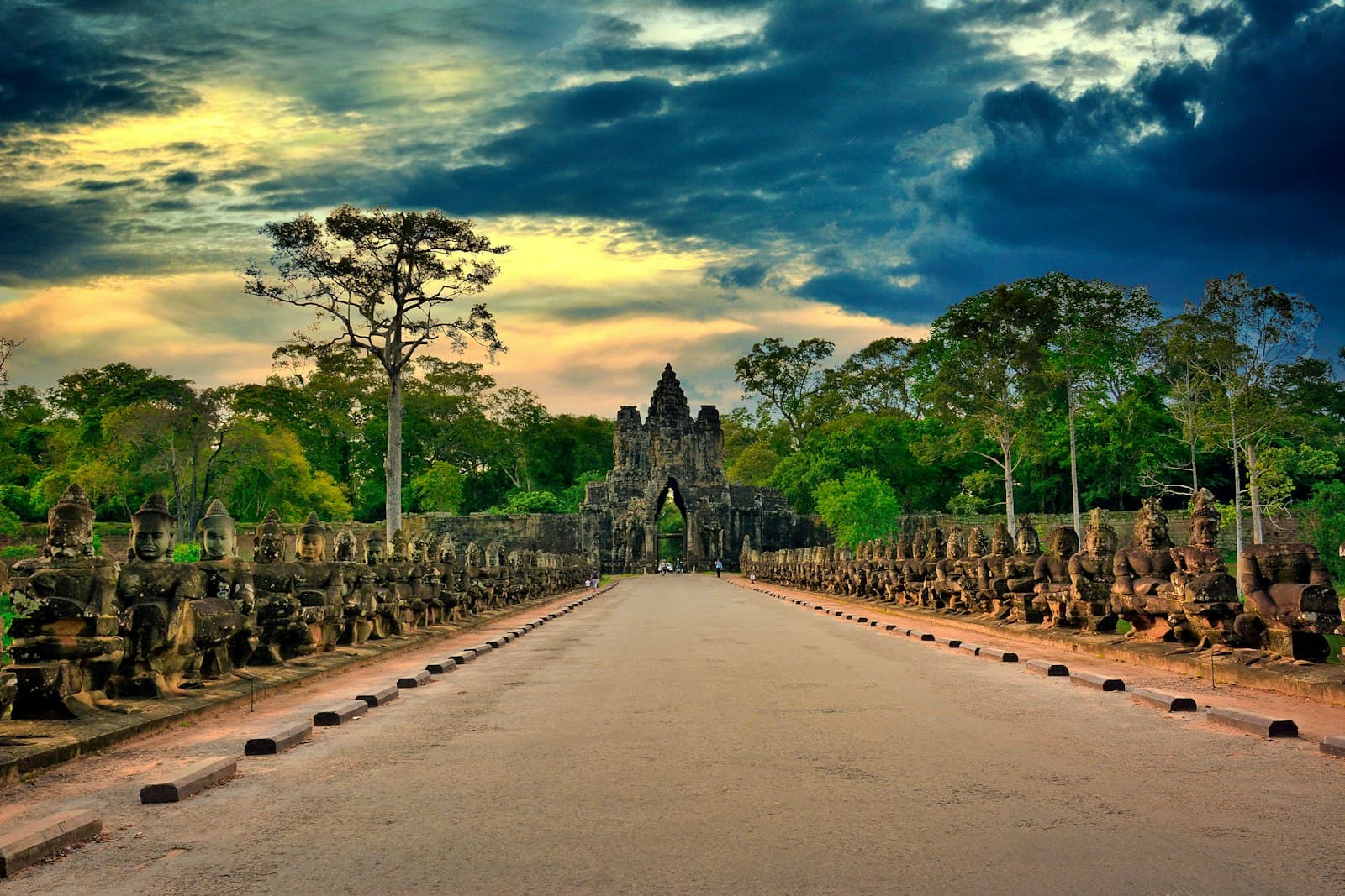 Banteay Srei — gray concrete road between green trees under blue sky and white clouds during daytime