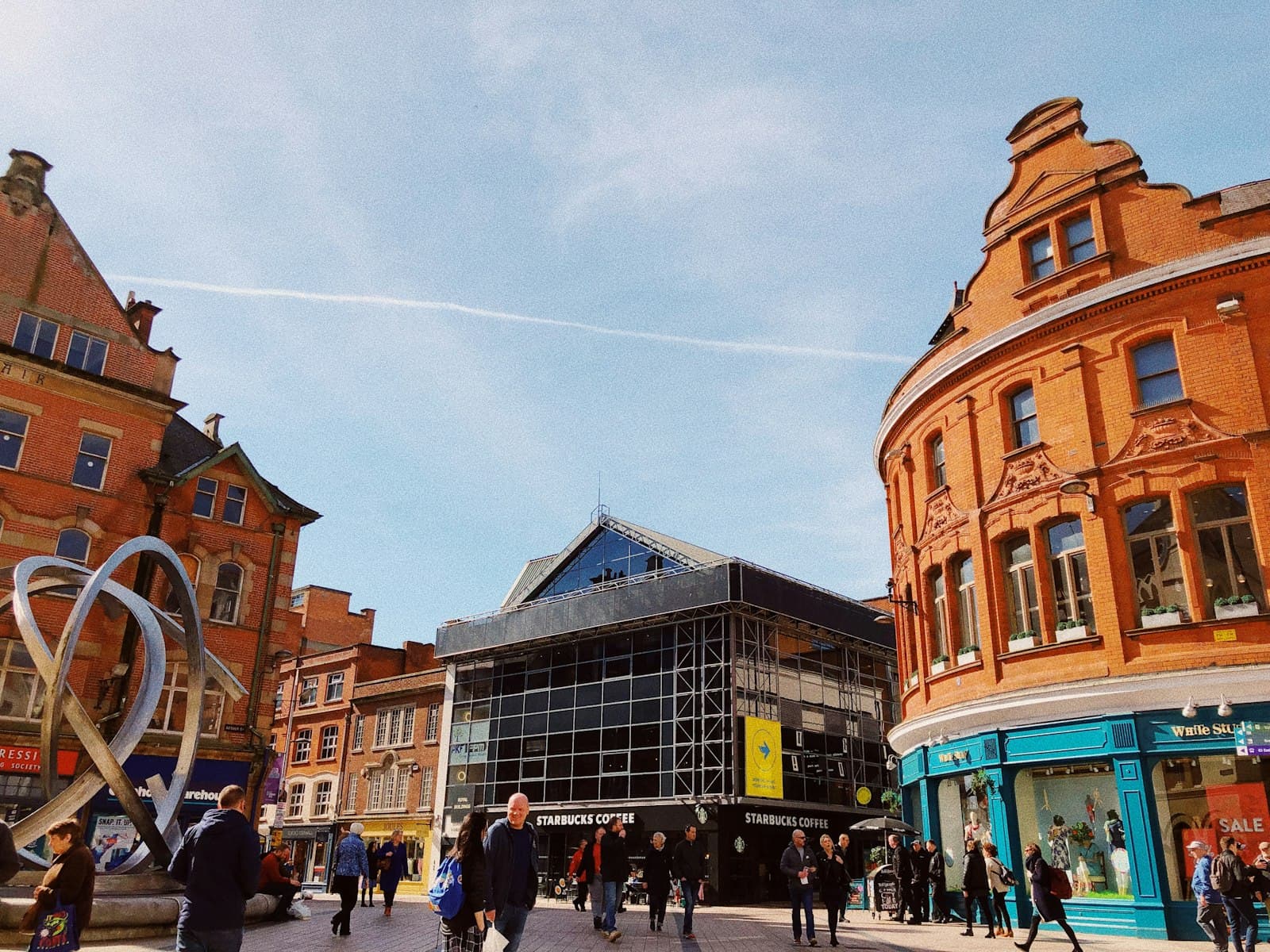 Belfast — people walking beside buildings under cloudy sky with contrail