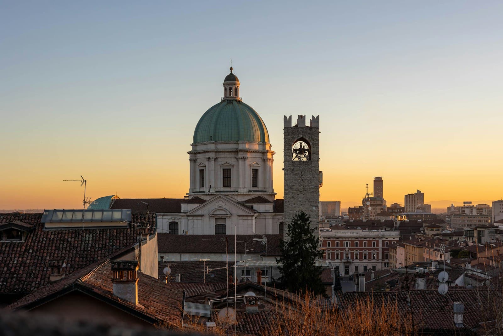 Brescia — a view of a city at sunset with a bell tower