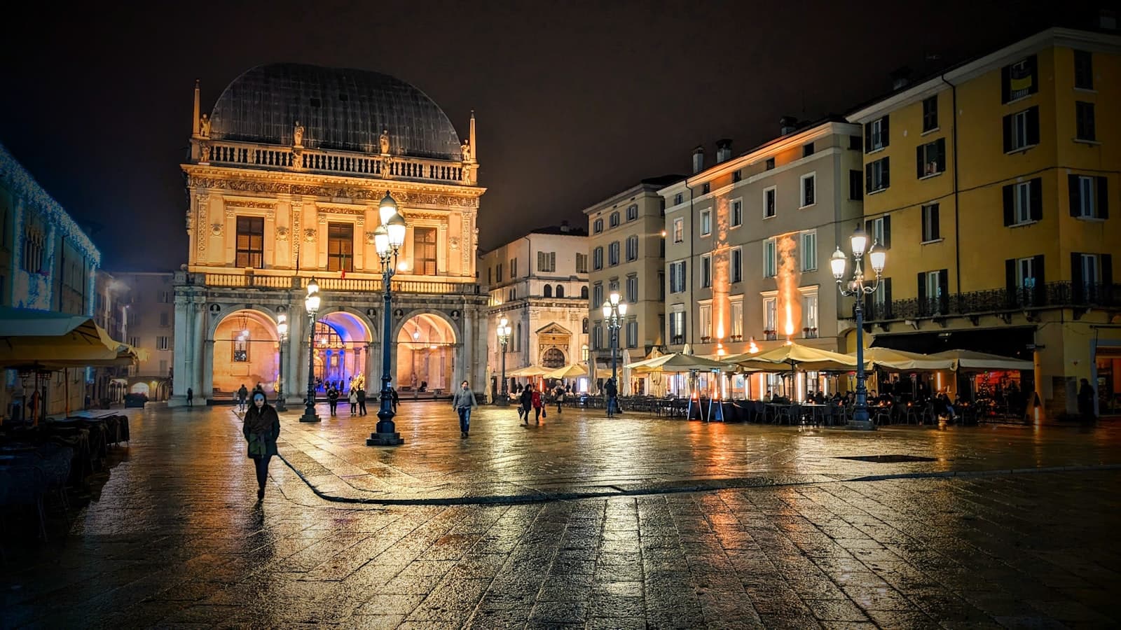 Brescia — a city square at night with people walking around