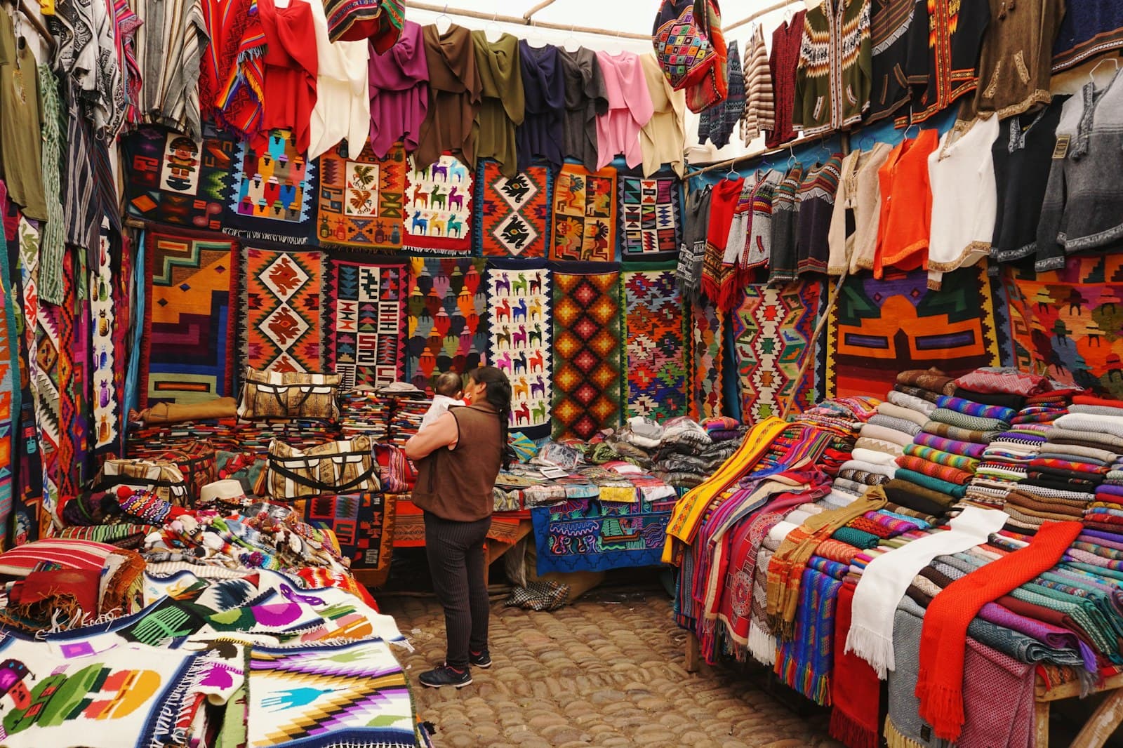 Cusco — woman in store with display of assorted shirts and textiles