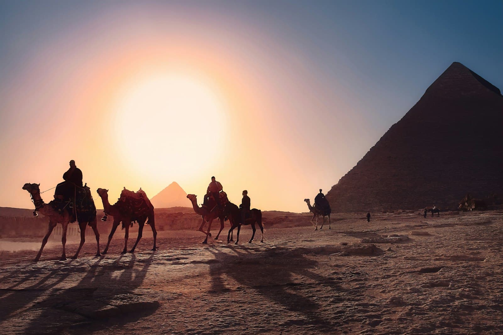 Dahab — five persons riding camels walking on sand beside Pyramid of Egypt