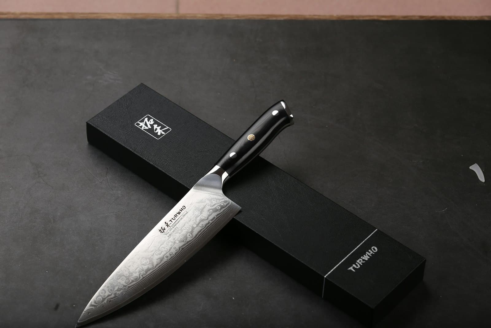 Damascus — A sharp chef's knife rests on its black box.