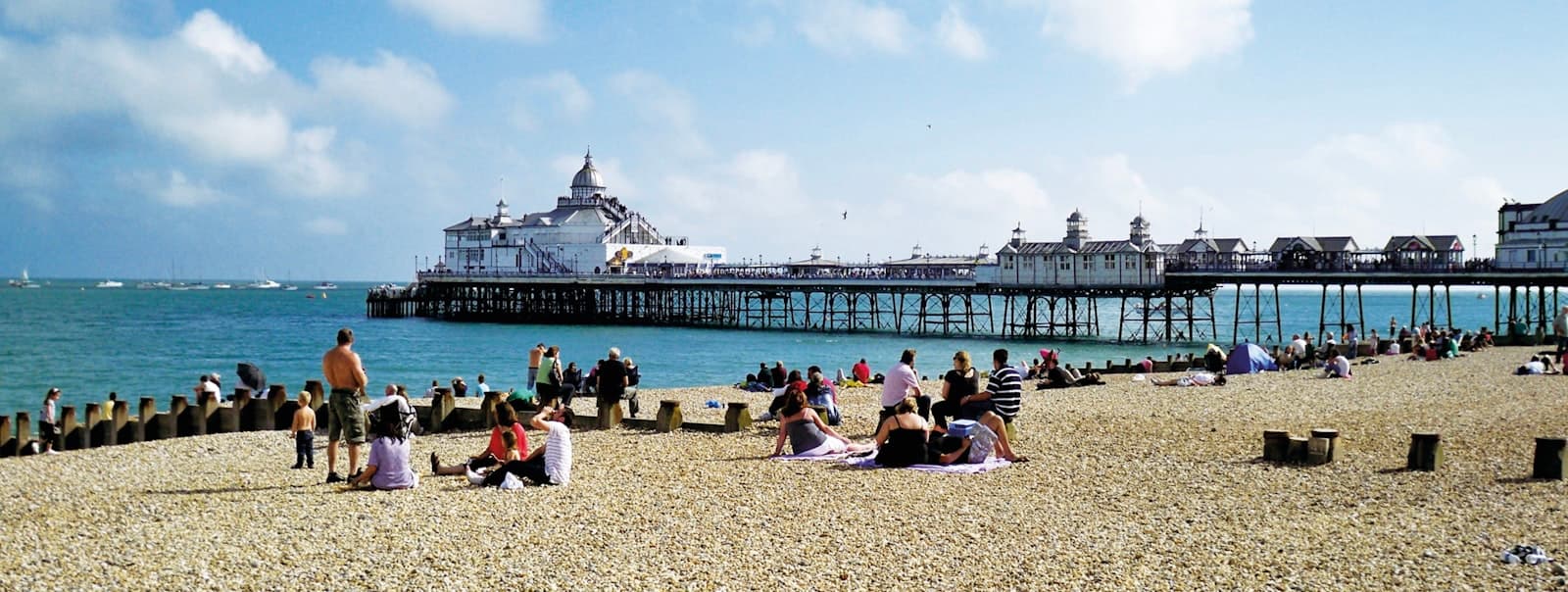 Eastbourne — people sitting on beach viewing buildings and hotels under white and blue sky