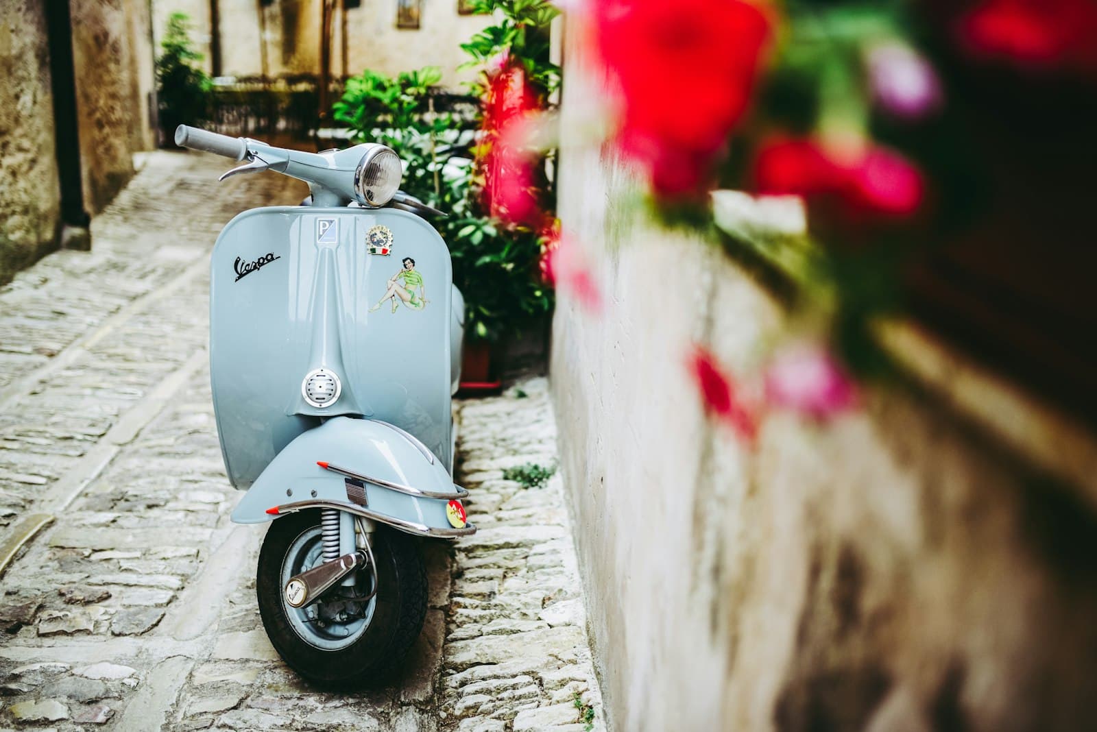 Erice — selective focus photo of blue motor scooter beside concrete wall
