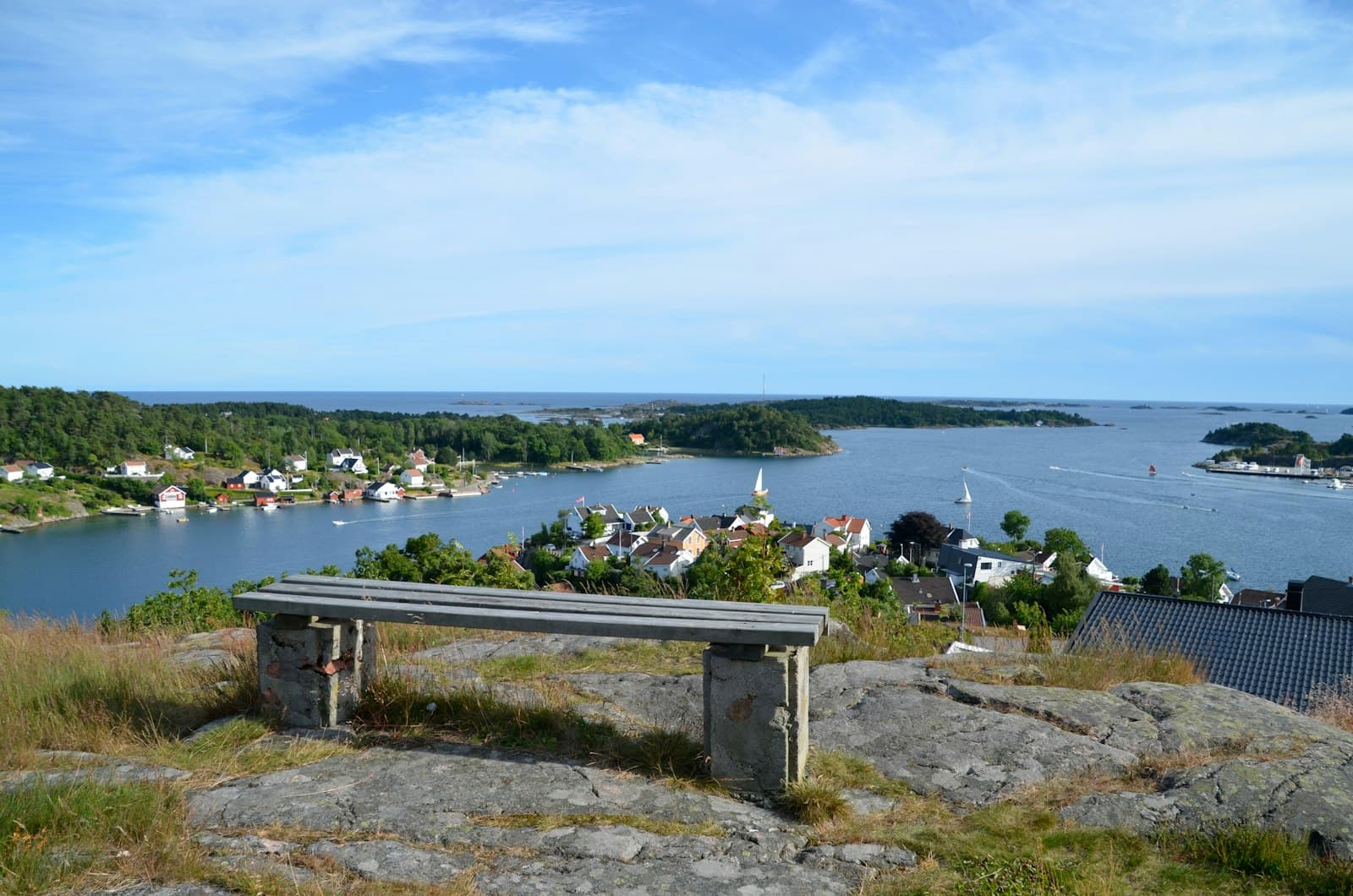Grimstad — a wooden bench sitting on top of a grass covered hillside
