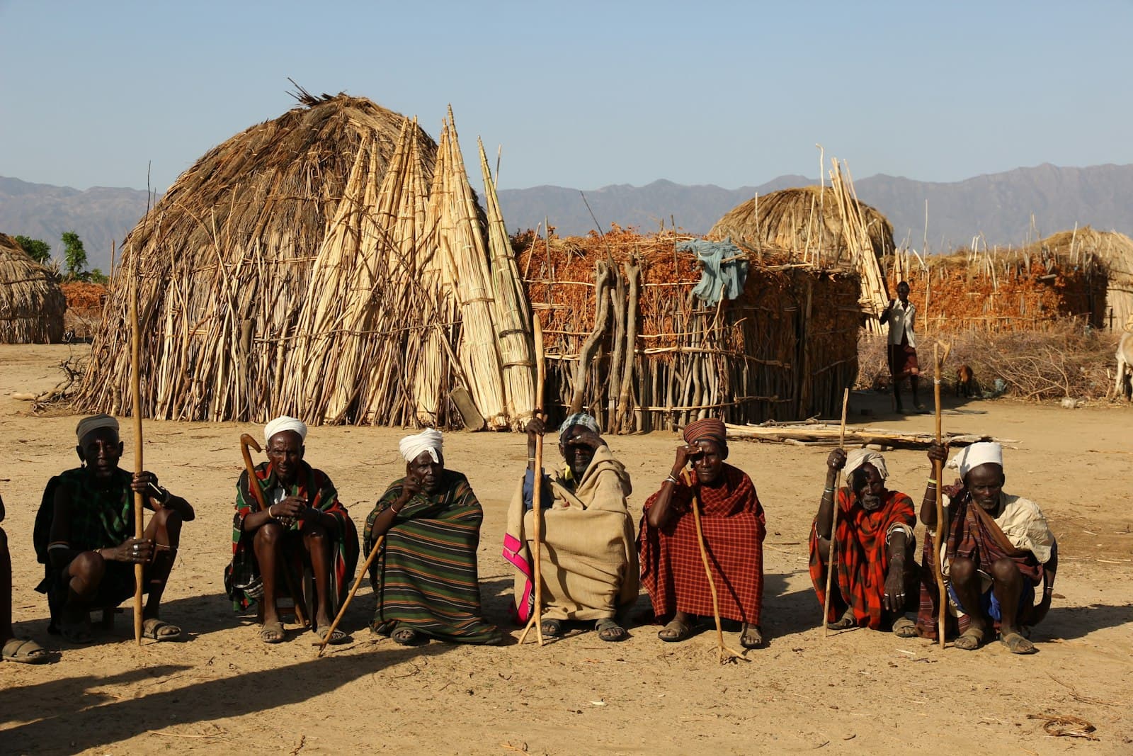 Hawassa — group of tribal men sitting on soil while holding sticks