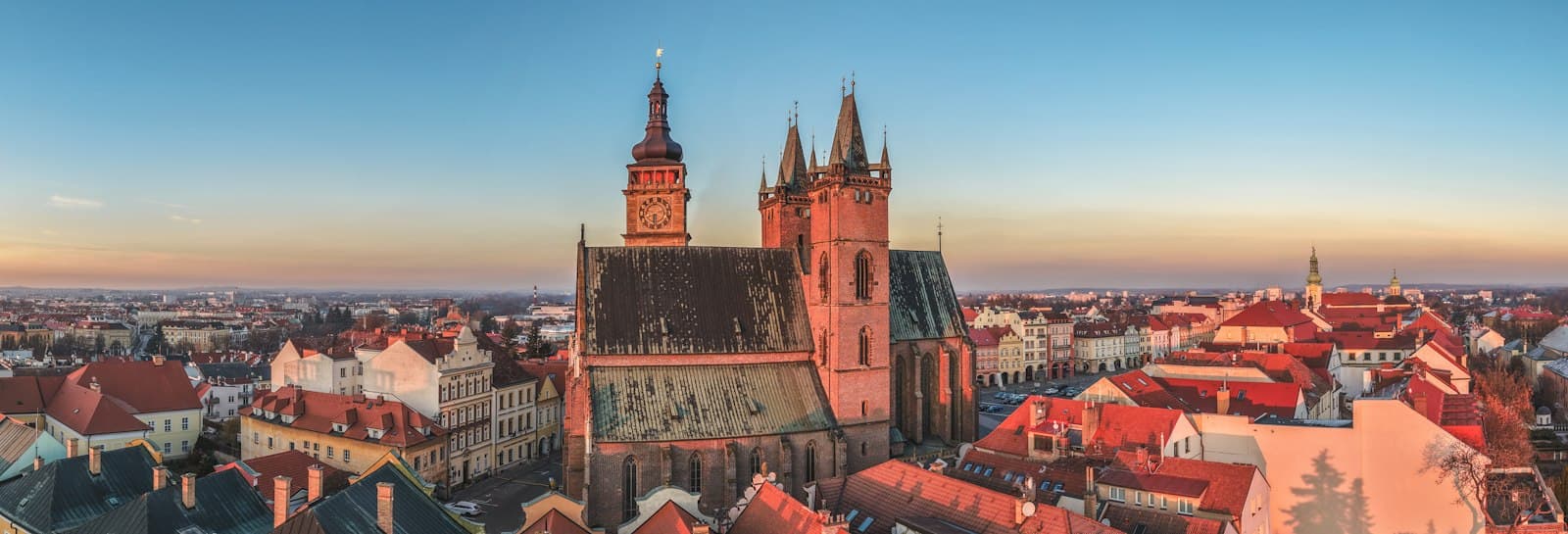 Hradec Králové — Historic church towers over red-roofed buildings at sunset