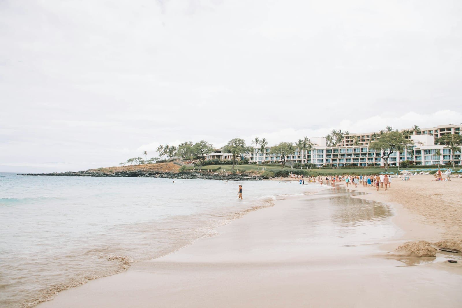 Kailua-Kona — a beach with people walking on it and buildings in the background