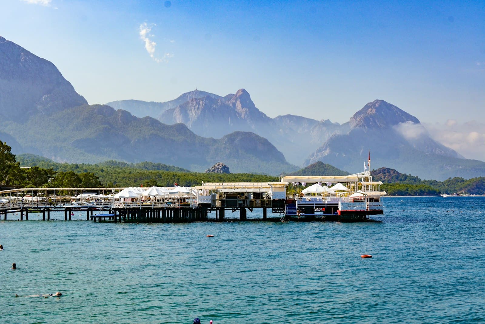 Kemer — a dock with boats and buildings by a body of water with mountains in the background