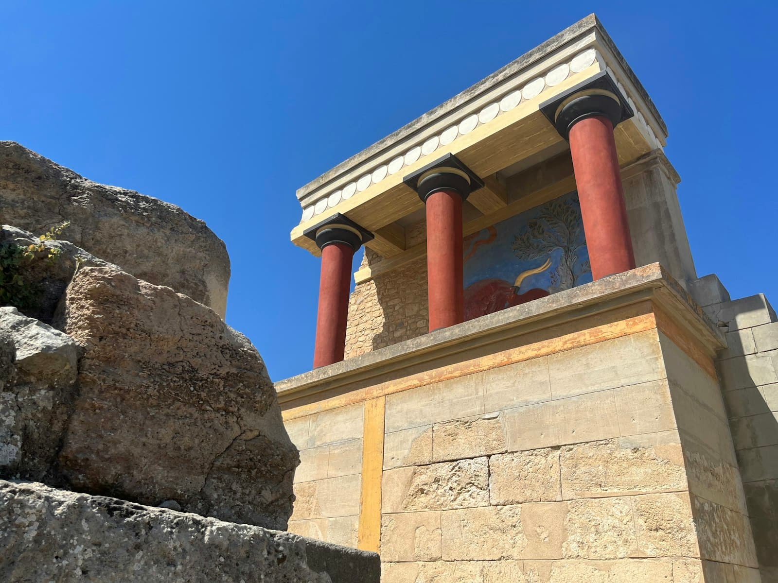Knossos — a stone building with two red pillars and a painting on the wall