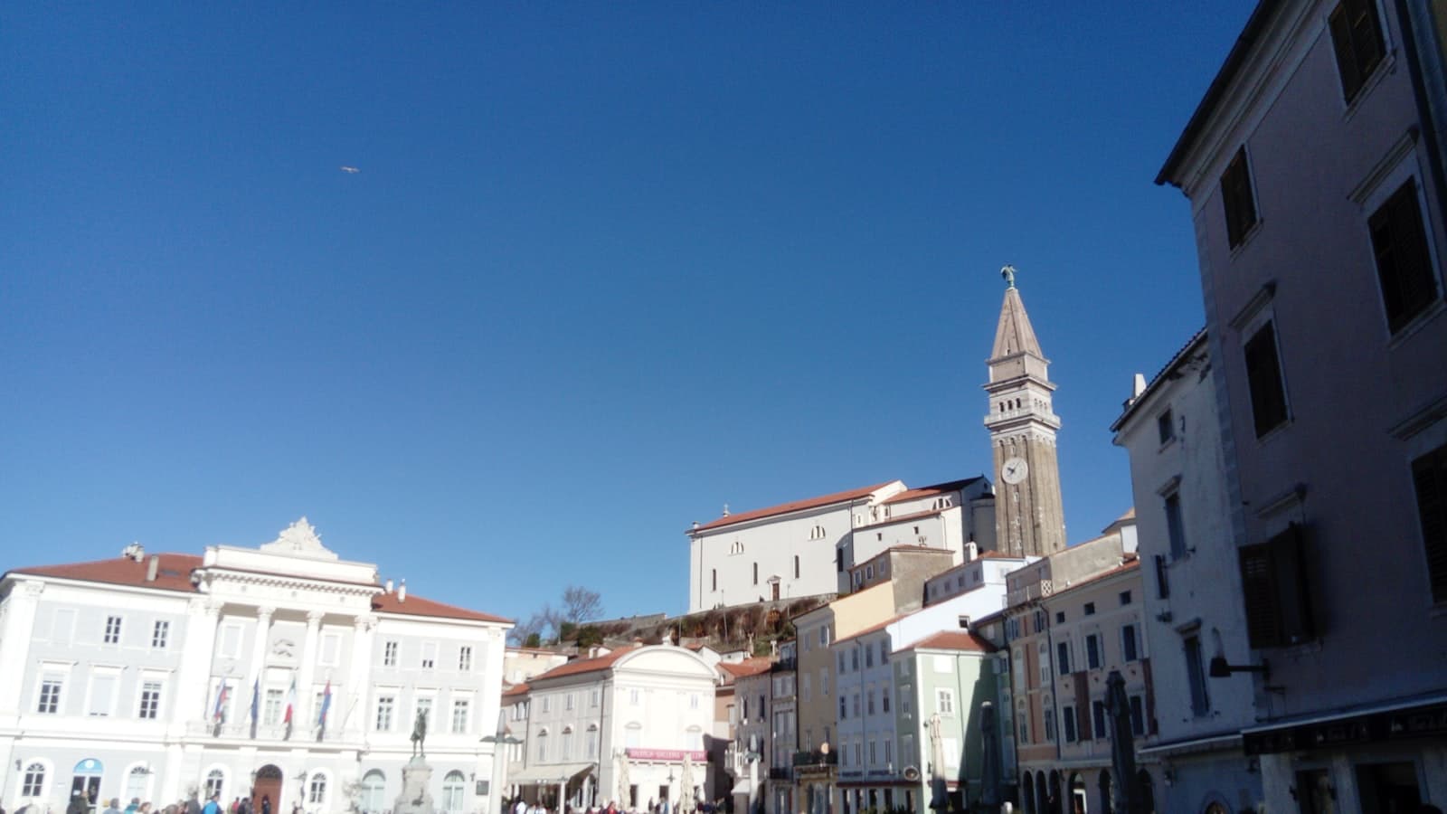 Koper — a group of people walking down a street next to tall buildings