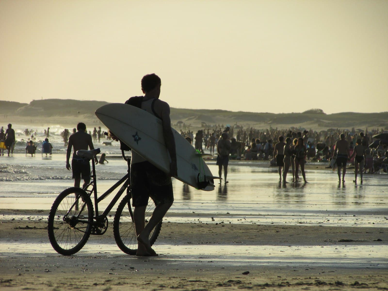 La Paloma — a man carrying a surfboard and a bike on a beach
