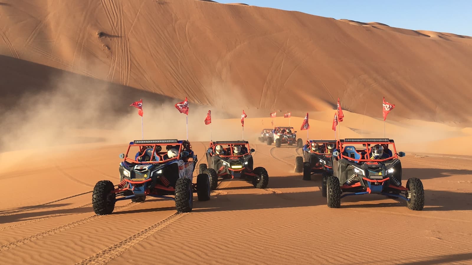 Liwa — three red monster trucks on sand dunes