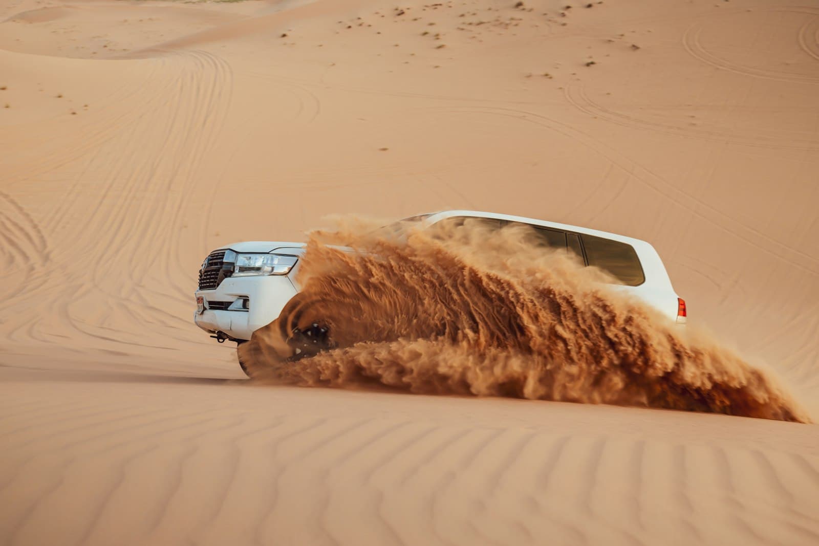 Liwa — A car kicks up sand in the desert.