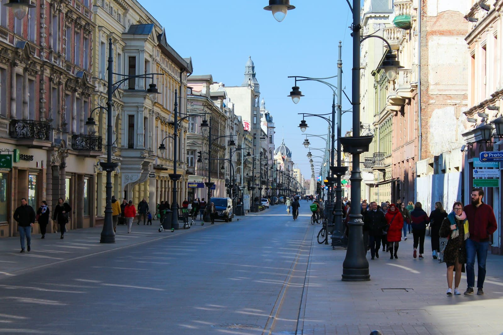 Łódź — a group of people walking down a street next to tall buildings
