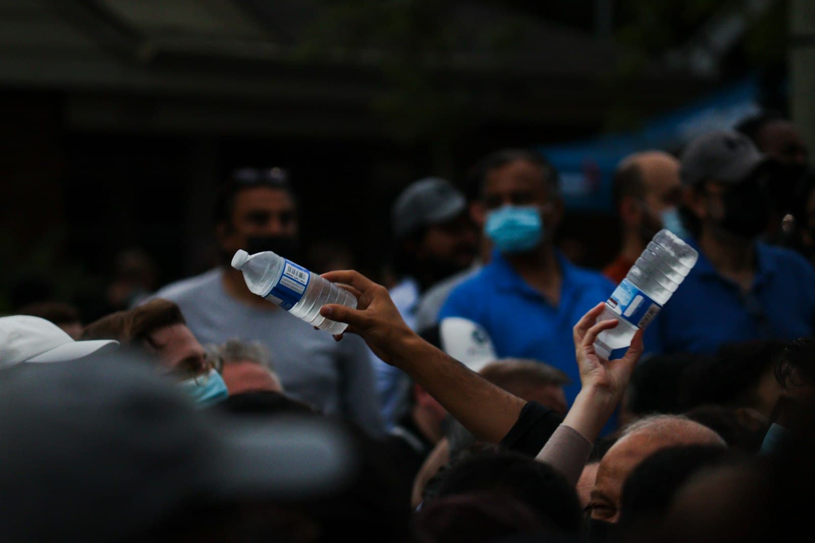 London — a crowd of people wearing face masks and holding up water bottles