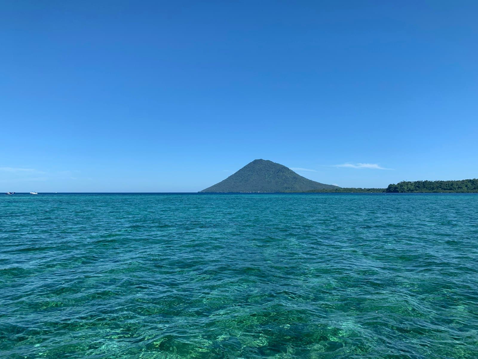 Manado — green sea near mountain under blue sky during daytime