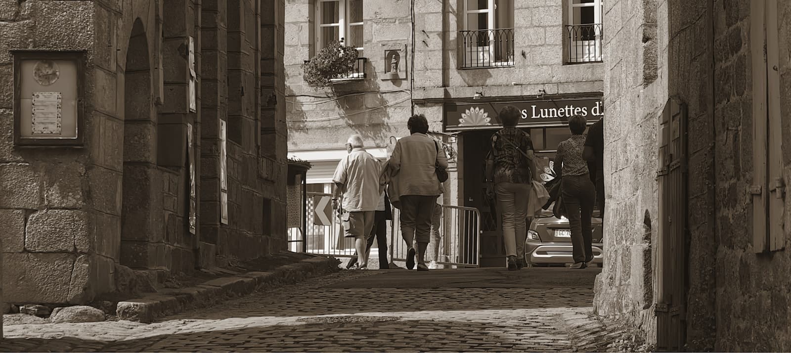 Moncontour — A couple of people walking down a street next to tall buildings