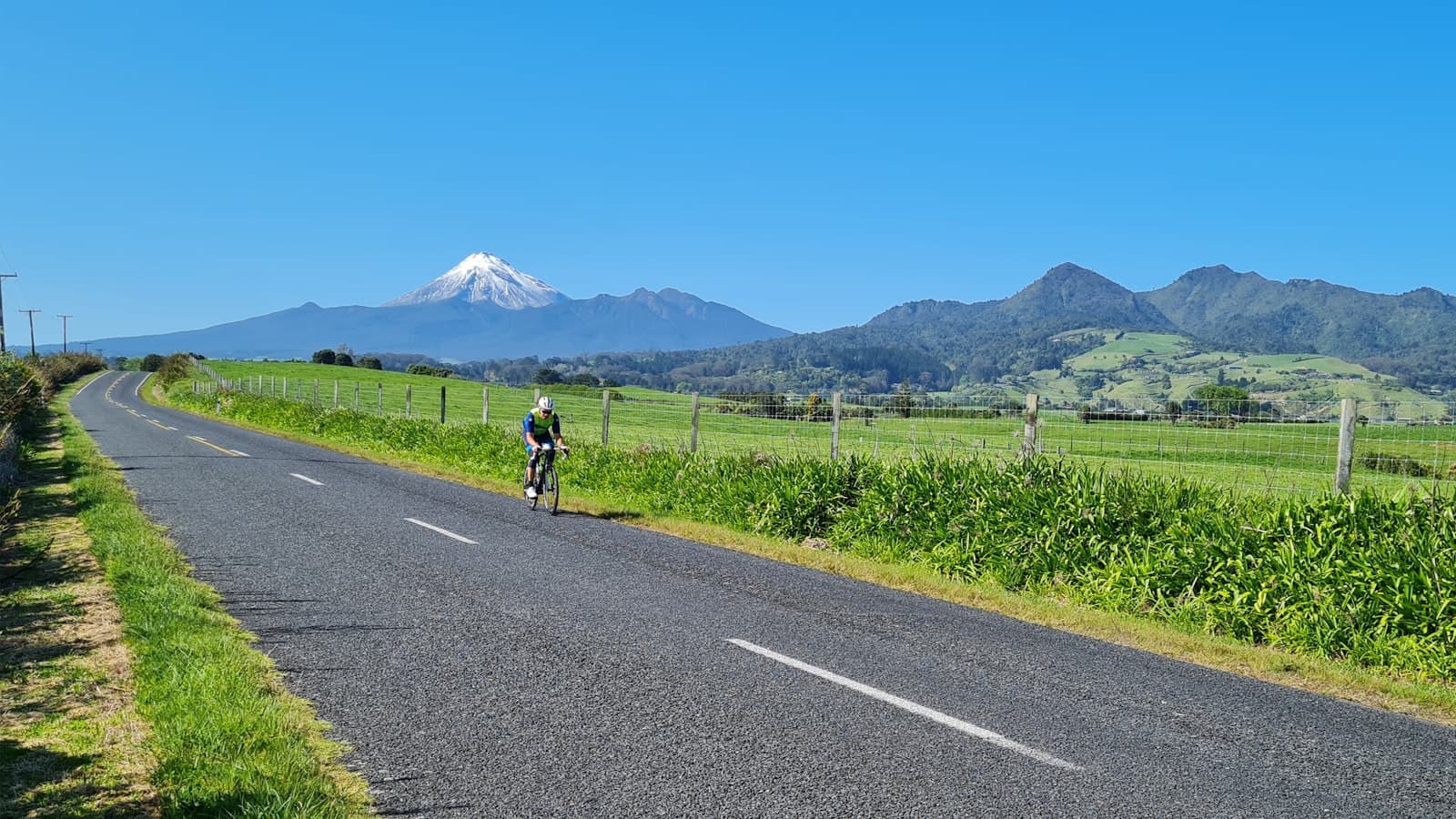 New Plymouth — a person riding a bicycle on a road with mountains in the background