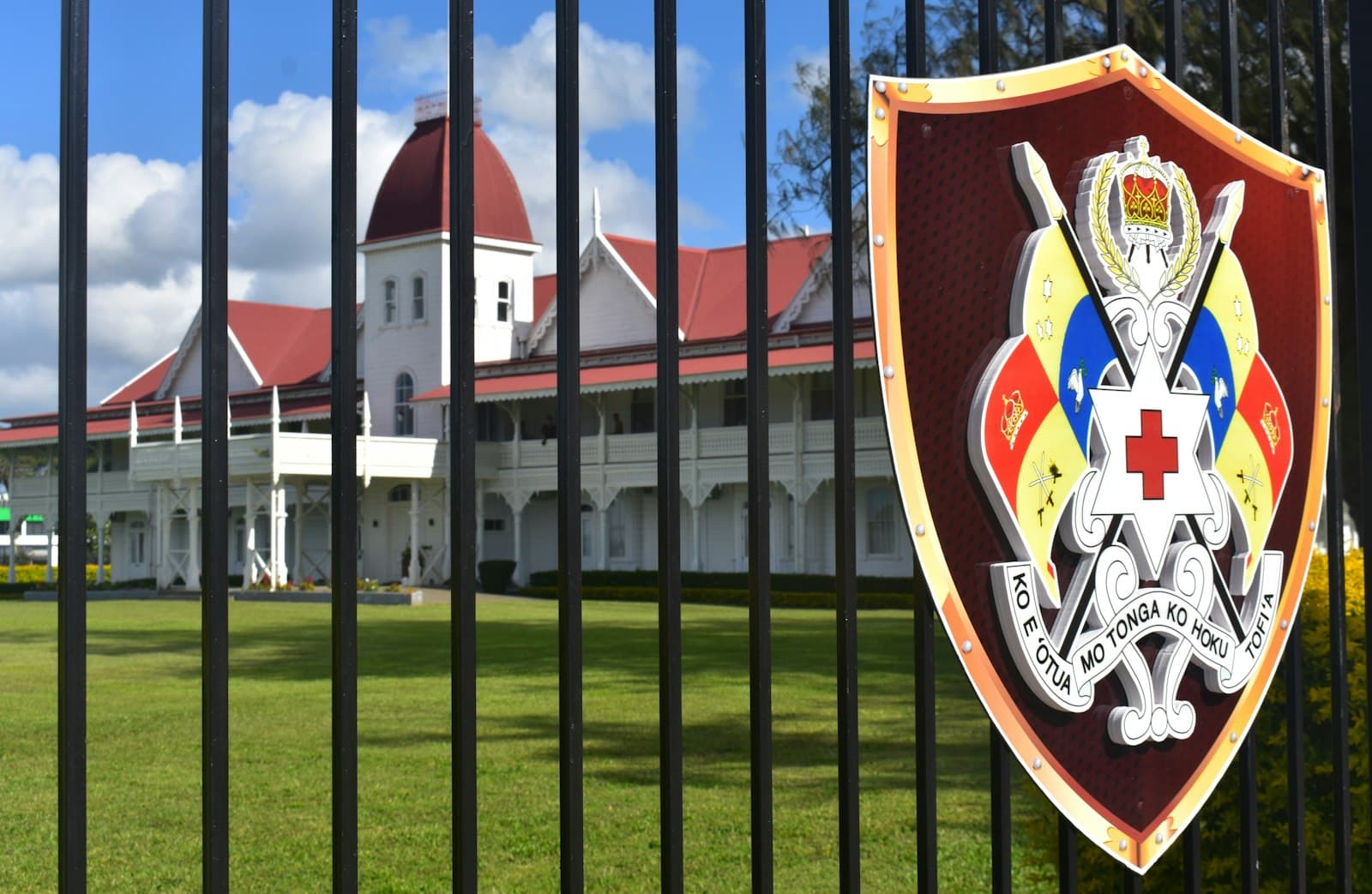 Nuku'alofa — Building with red roof behind a fence displaying an emblem.