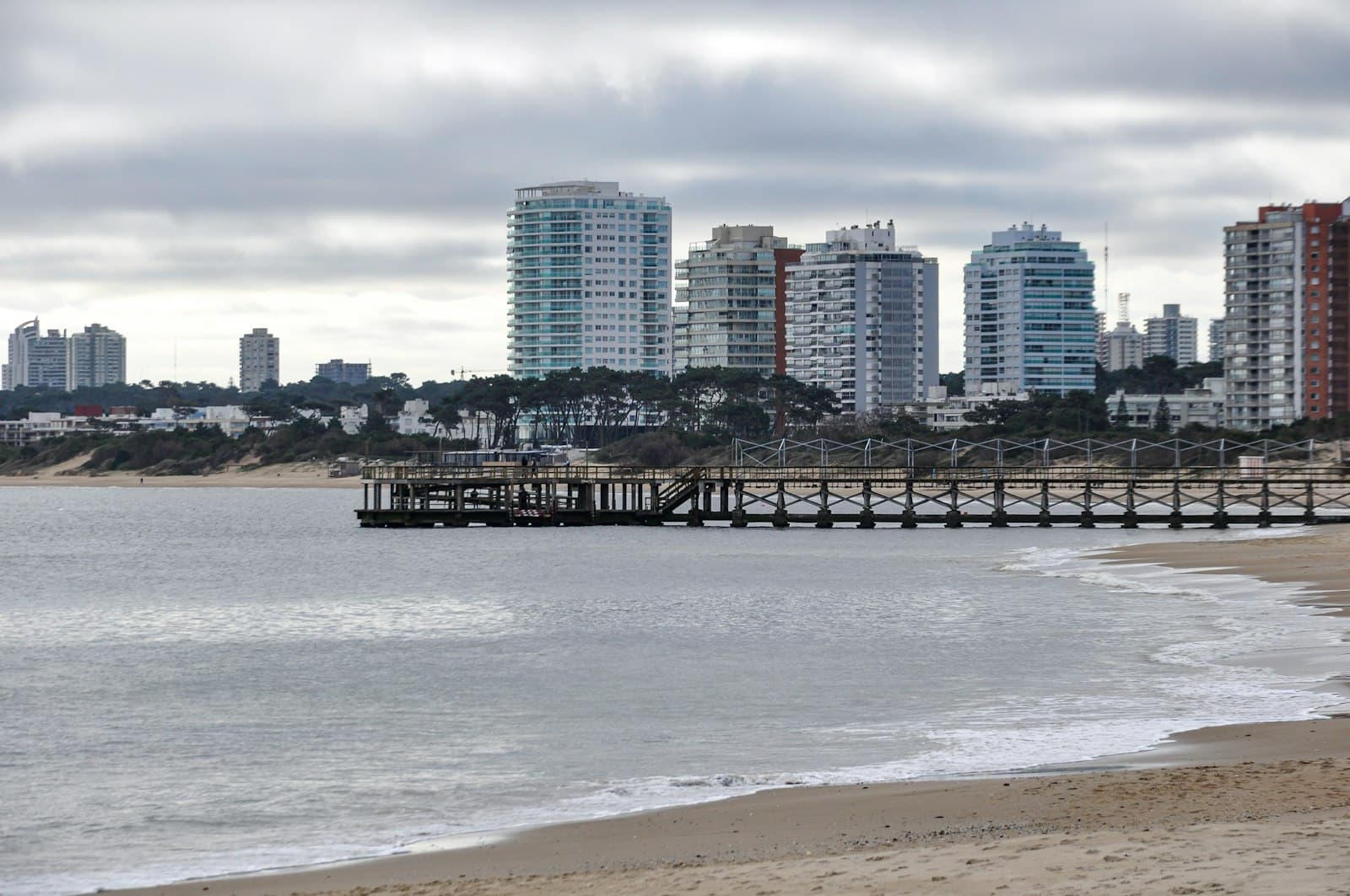Paysandú — City skyline, pier, and sandy beach under a cloudy sky.