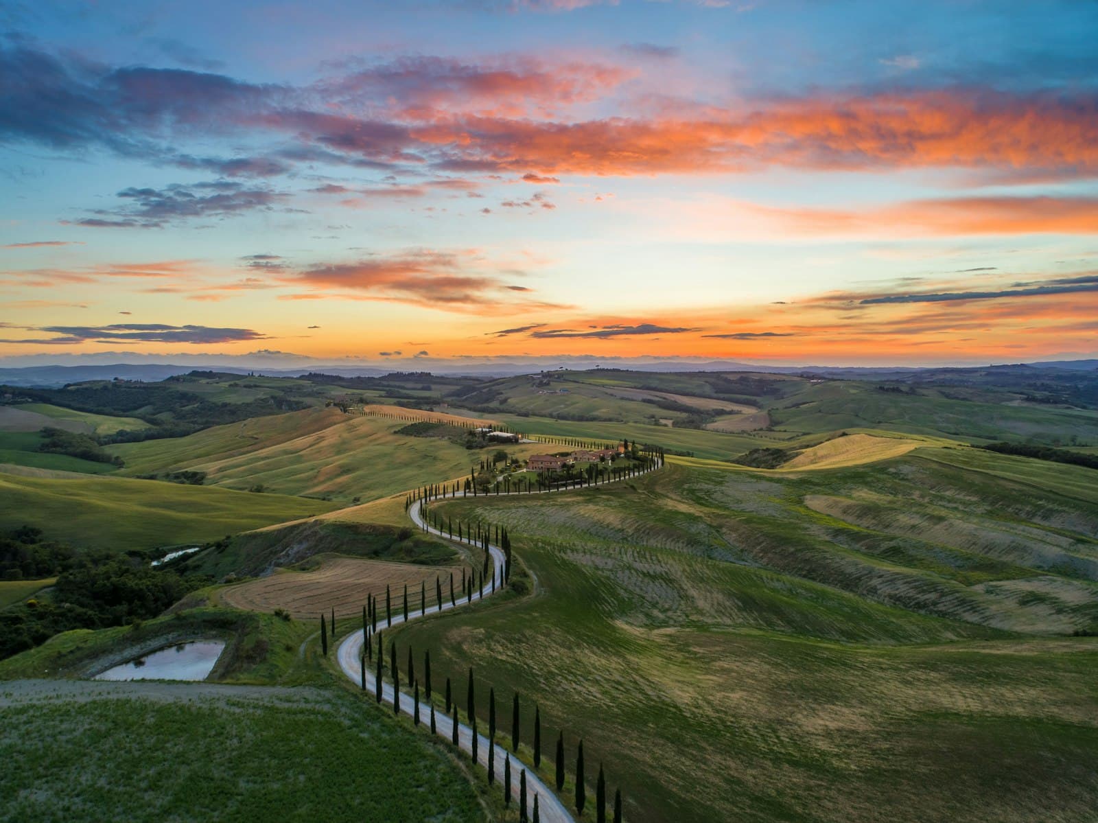 San Quirico d'Orcia — road between green grass field near mountains under blue and brown sky at golden hour