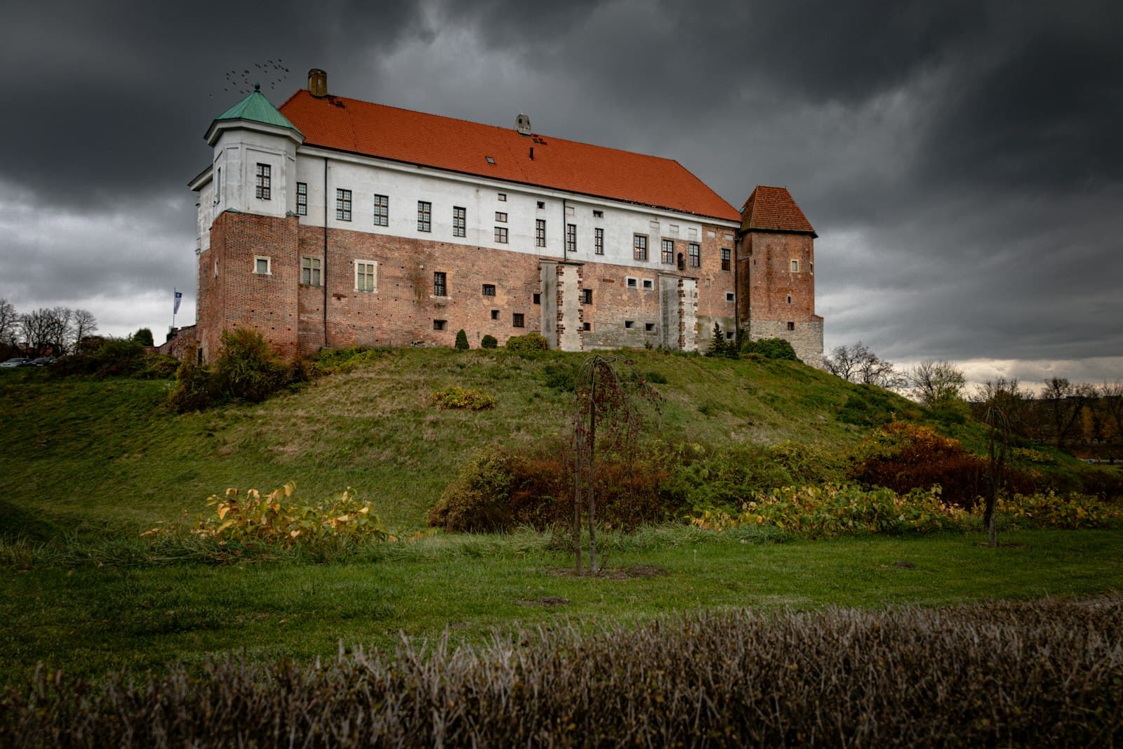 Sandomierz — a large building sitting on top of a lush green hillside
