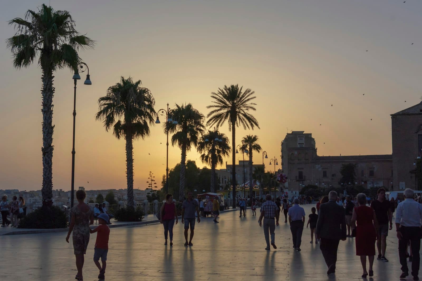 Sciacca — a group of people walking down a street next to palm trees