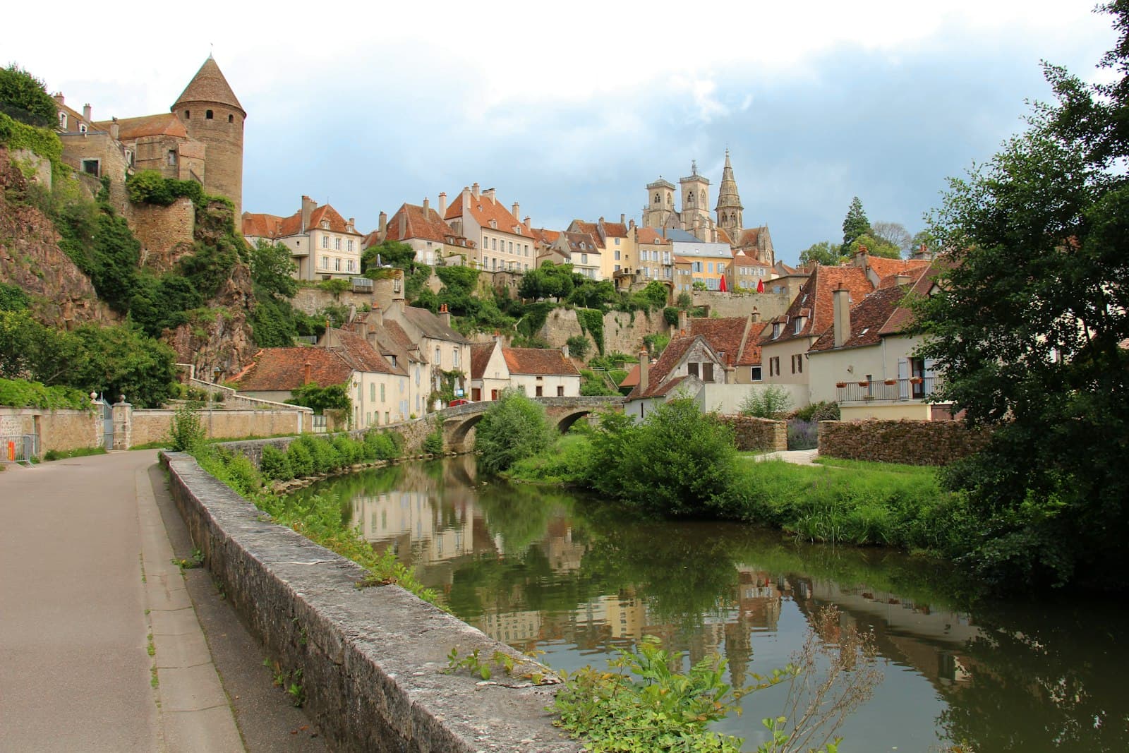 Semur-en-Auxois — a river running through a village next to a lush green hillside