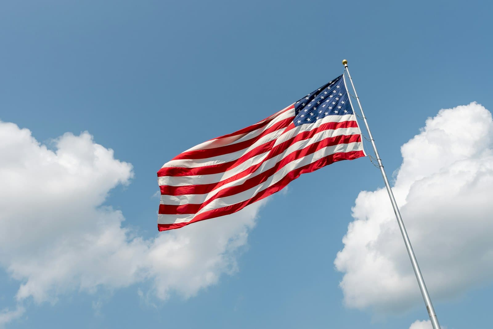 Sioux Falls — American flag waving against a blue sky with white clouds.