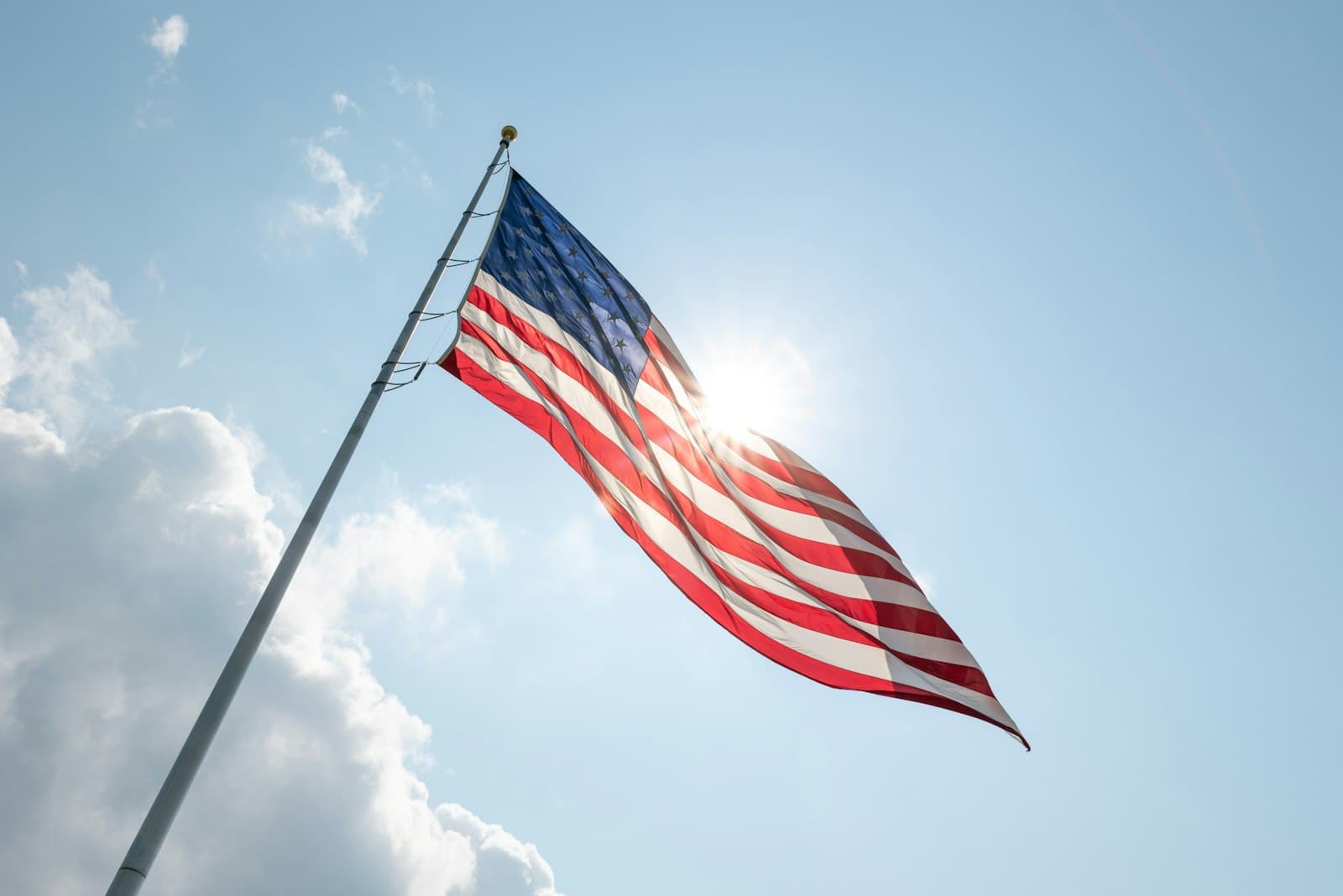 Sioux Falls — American flag waving against a bright blue sky with sun.