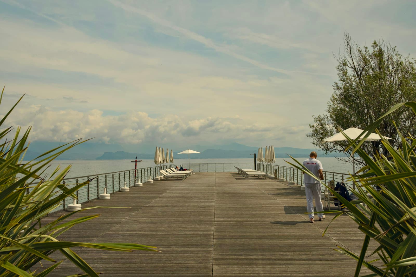 Sirmione — Man walks on a pier towards a calm lake.