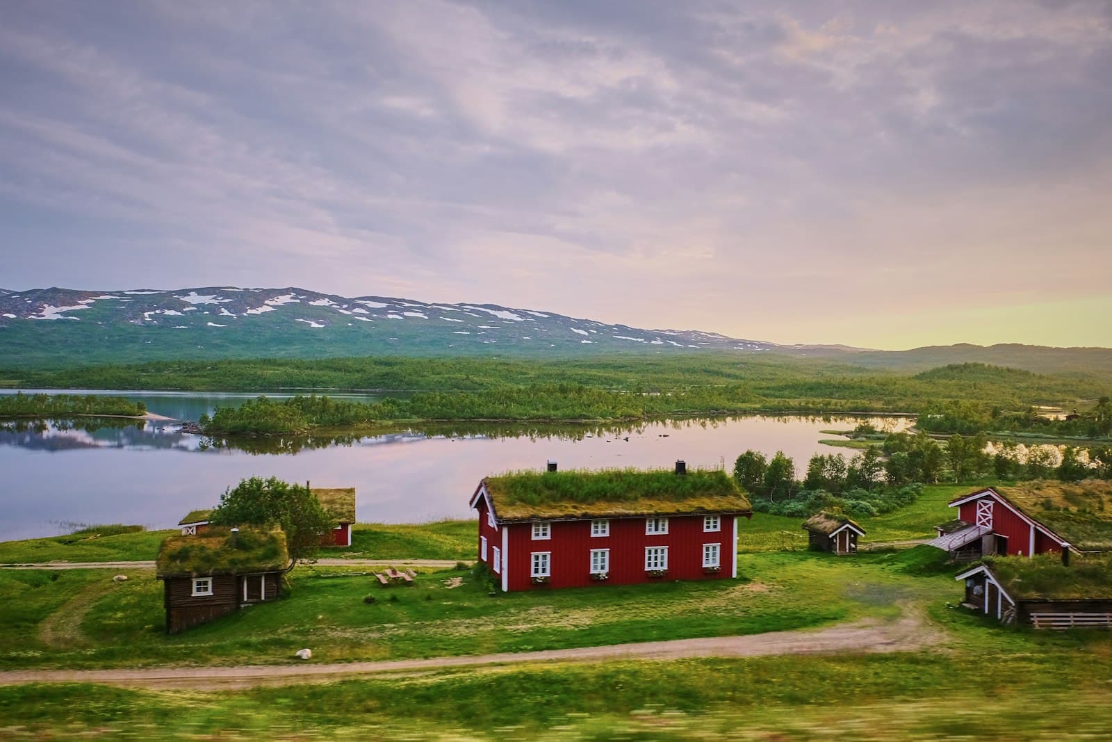 Skellefteå — Red wooden houses with grass roofs near a lake and snow-capped mountains
