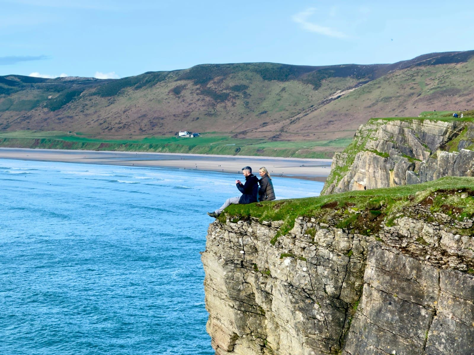 Swansea — two people sitting on a cliff overlooking a body of water
