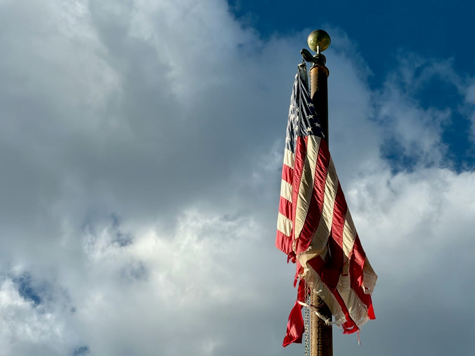 Taos — Tattered american flag waves against a cloudy sky