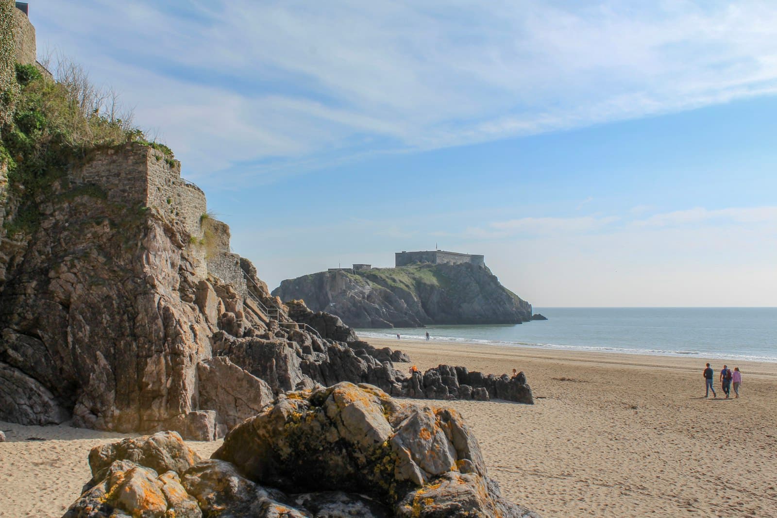 Tenby — brown rocky mountain beside sea under blue sky during daytime