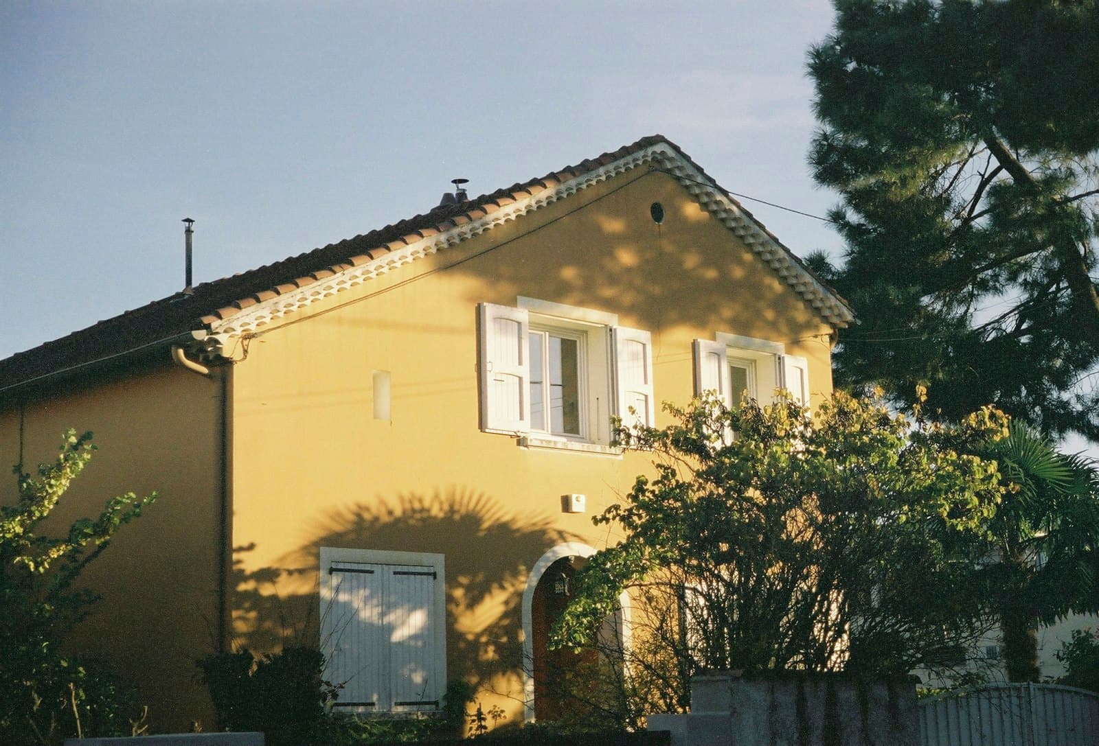 Valence — a yellow house with white shutters and a tree in front of it