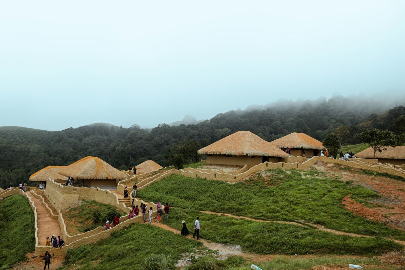 Wayanad — a group of people walking around a grass field with huts